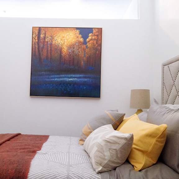 a bedroom with a bed, a lamp, and a painting of a forest.